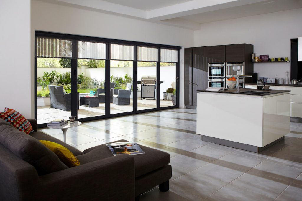 Interior view of Origin aluminium bifold doors connecting the kitchen and living room, enhancing natural light and providing seamless access to the outdoor area, ideal for homes in {location}.